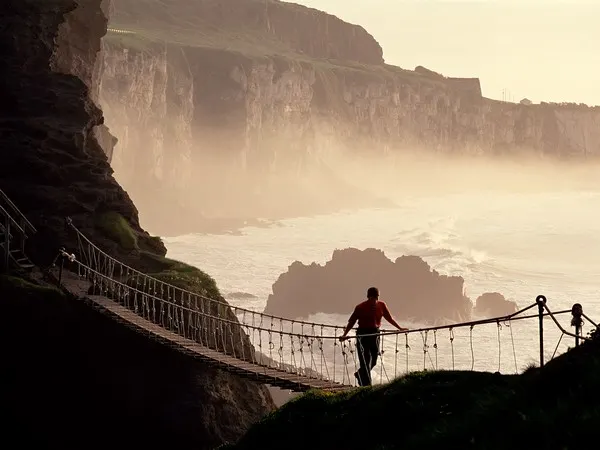 A man walks a rope bridge over a turbulent sea in County Antrim, Ireland